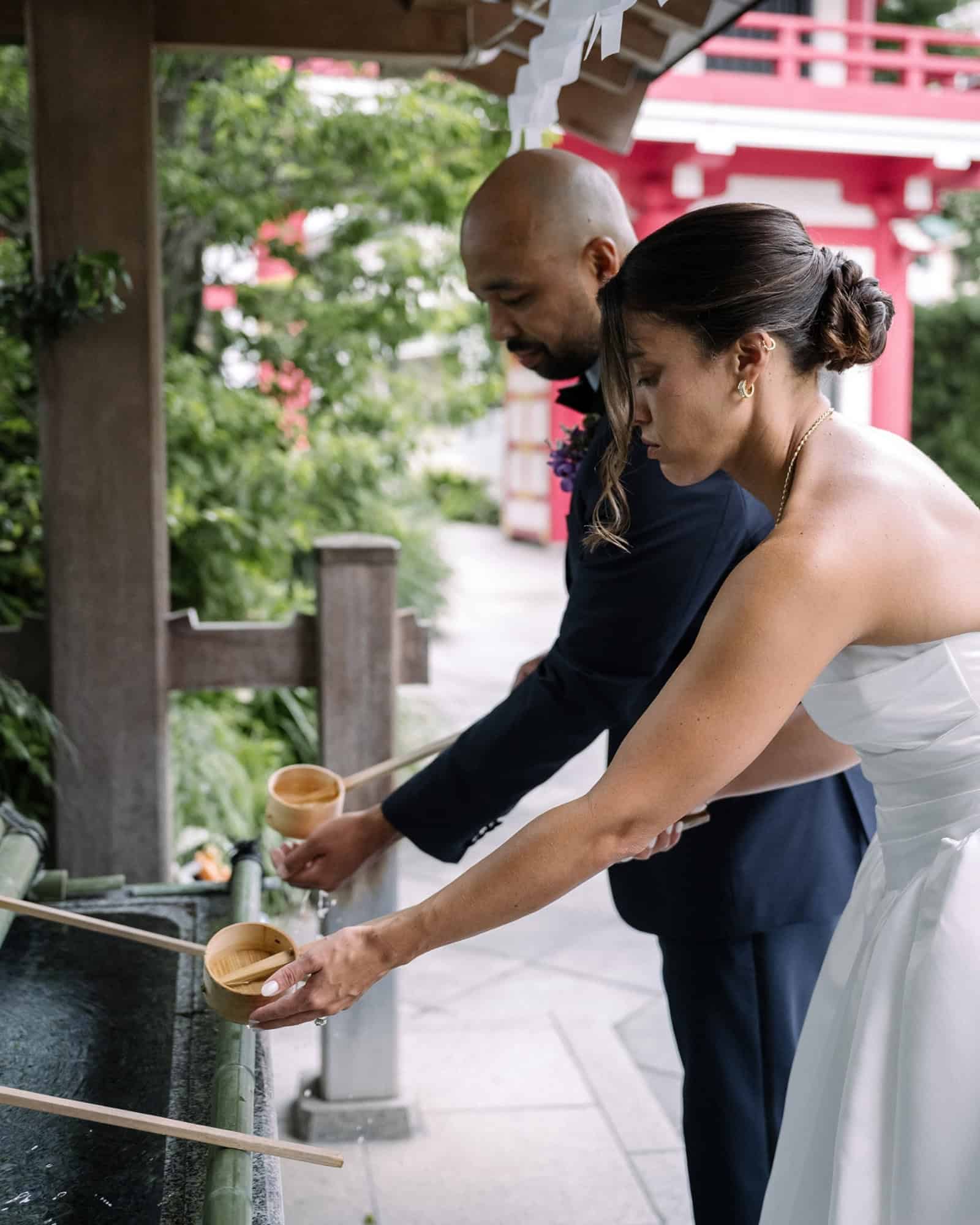 A couple rinse their hands with wooden ladles at a shrine water basin in Tokyo before a Shinto blessing, Japanese wedding etiquette.