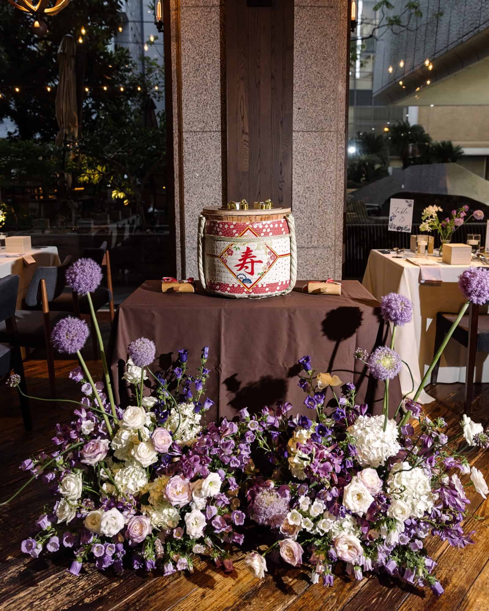 A sake barrel marked kotobuki, for celebration, waits among purple and white flowers for kagami biraki at a wedding reception in Tokyo.