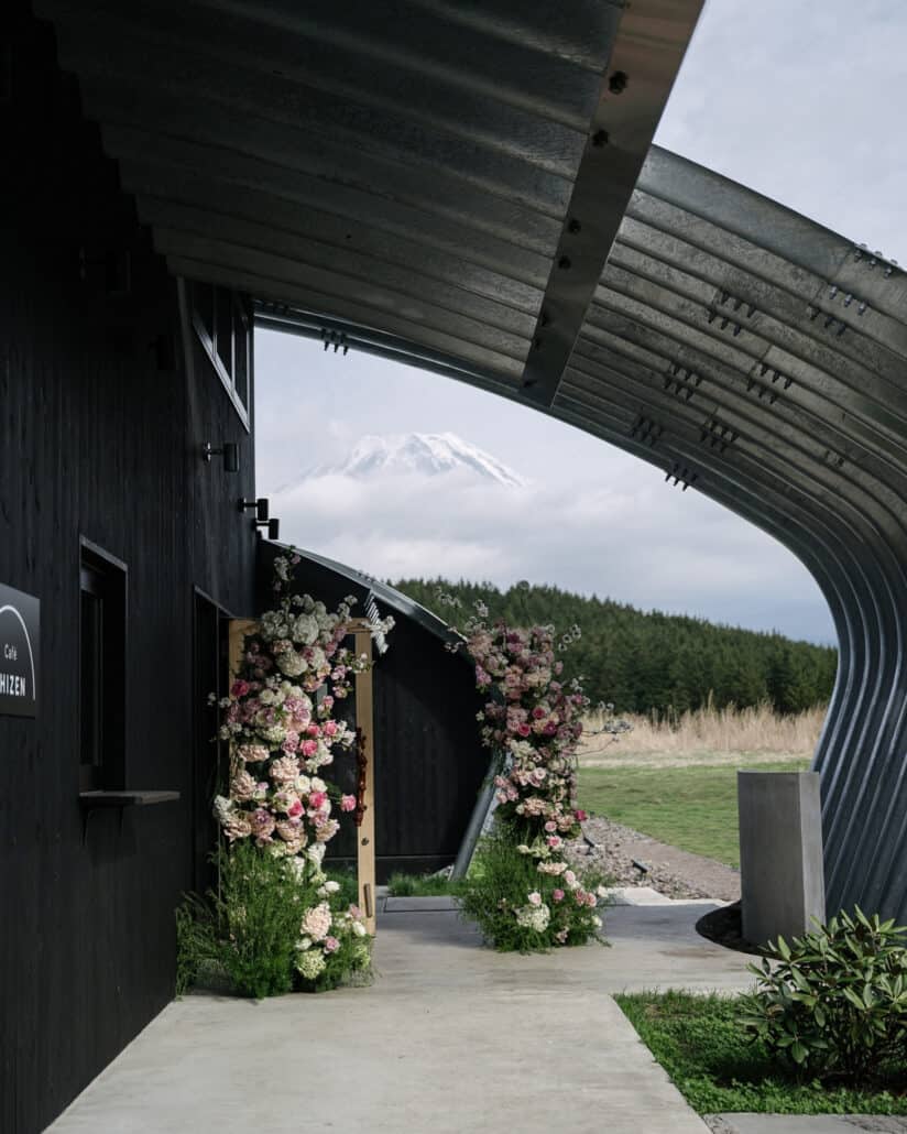 Floral columns frame the doorway of Cafe Shizen at Fujisan Winery, a unique wedding venue at Mt Fuji, the mountain in cloud beyond the steel arch.