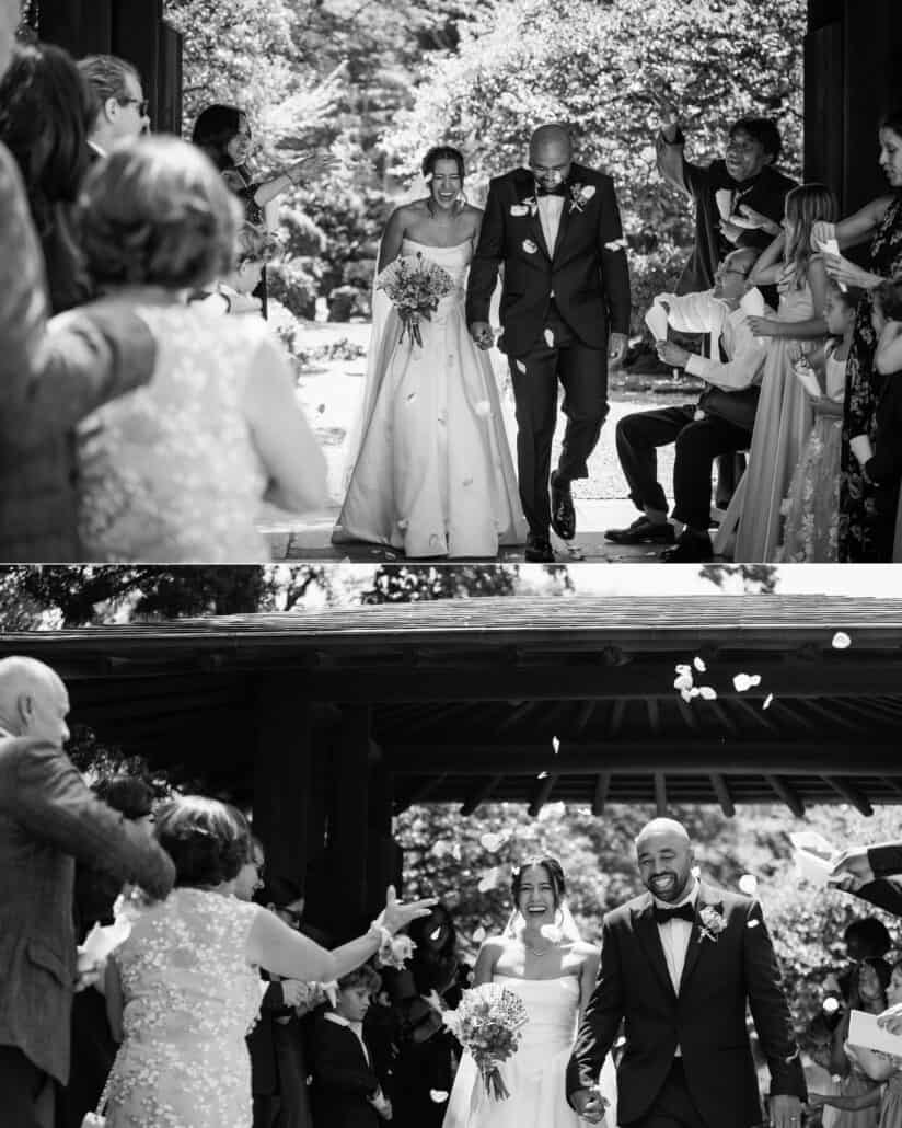 In black and white, guests throw petals as the just married couple walk back down the aisle and out through the old wooden gate.