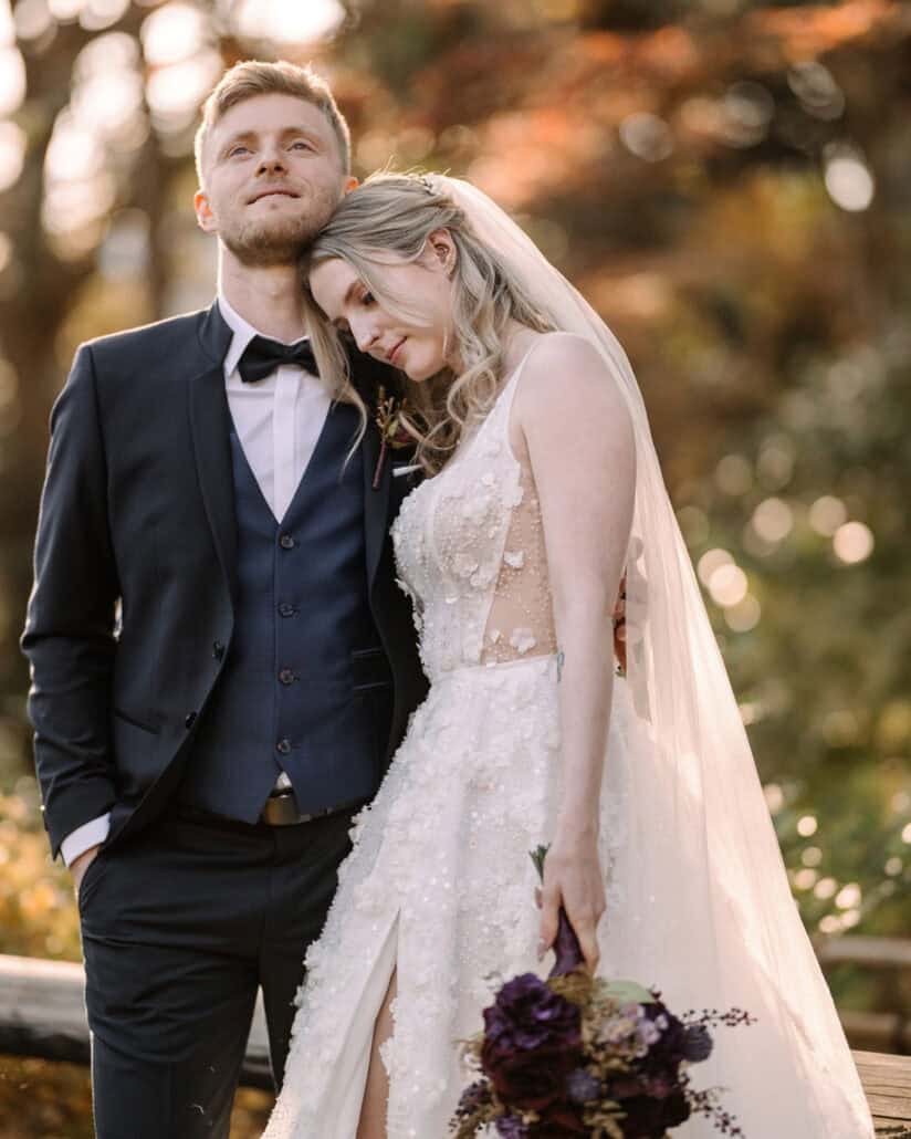 The bride leans her head against the groom, a dark purple bouquet in her hand, in golden light at their autumn elopement in Japan.