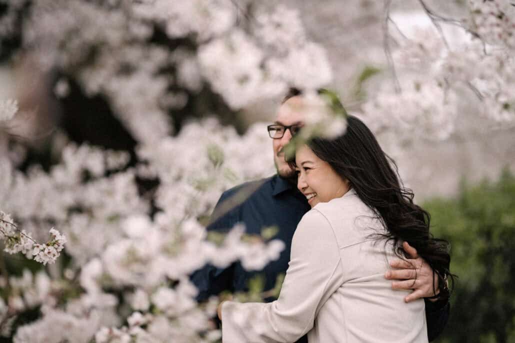 She laughs as the couple embrace behind a screen of cherry blossoms in a Tokyo park, on their pre-wedding shoot before the wedding in Japan.