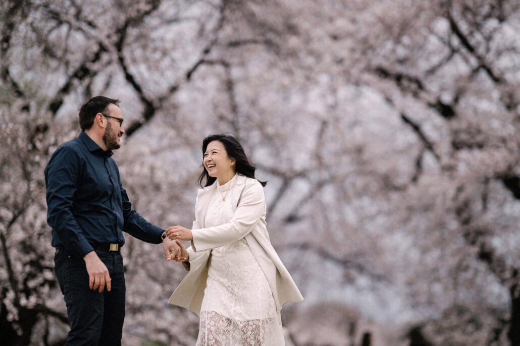 She laughs as they hold hands for a small dance under cherry trees in full bloom in a Tokyo park, her cream coat swinging.