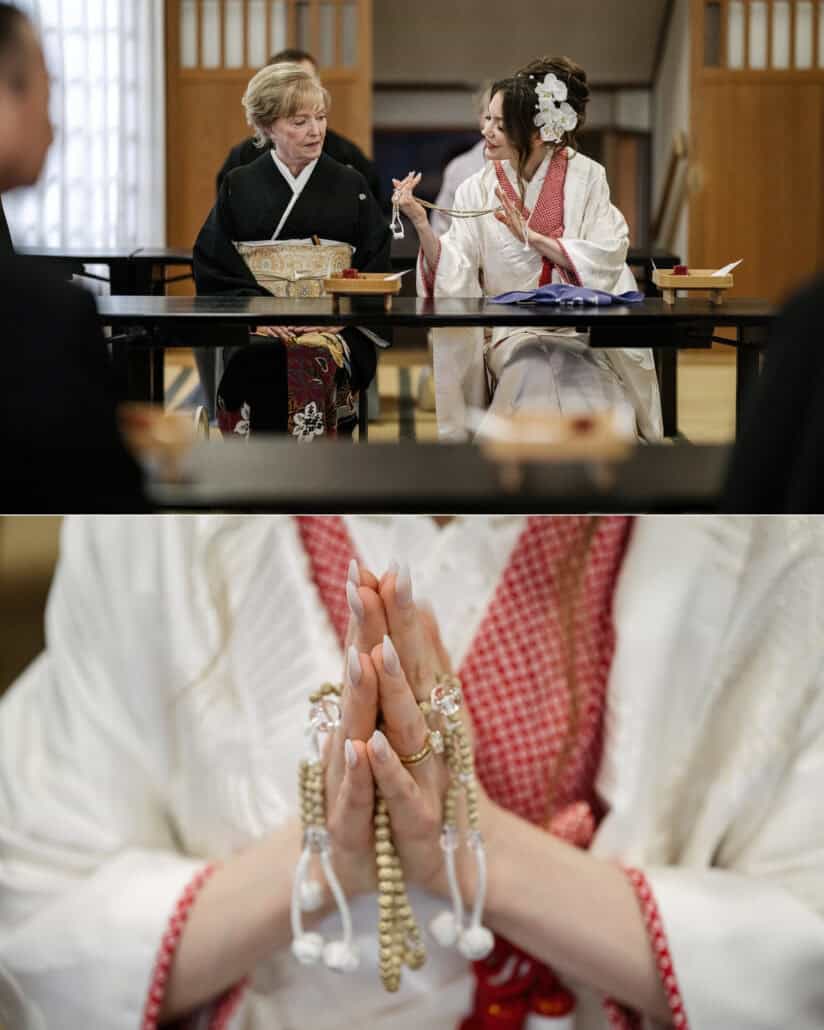 The bride and a woman in black kimono turn to each other at the ceremony table, and the bride's hands press together around Buddhist prayer beads.