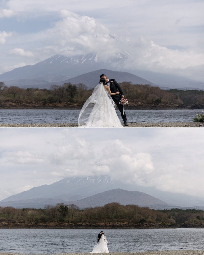 The couple kiss on the shore of Lake Shoji as her veil lifts in the wind, then stand small at the water's edge below Mt Fuji in cloud.