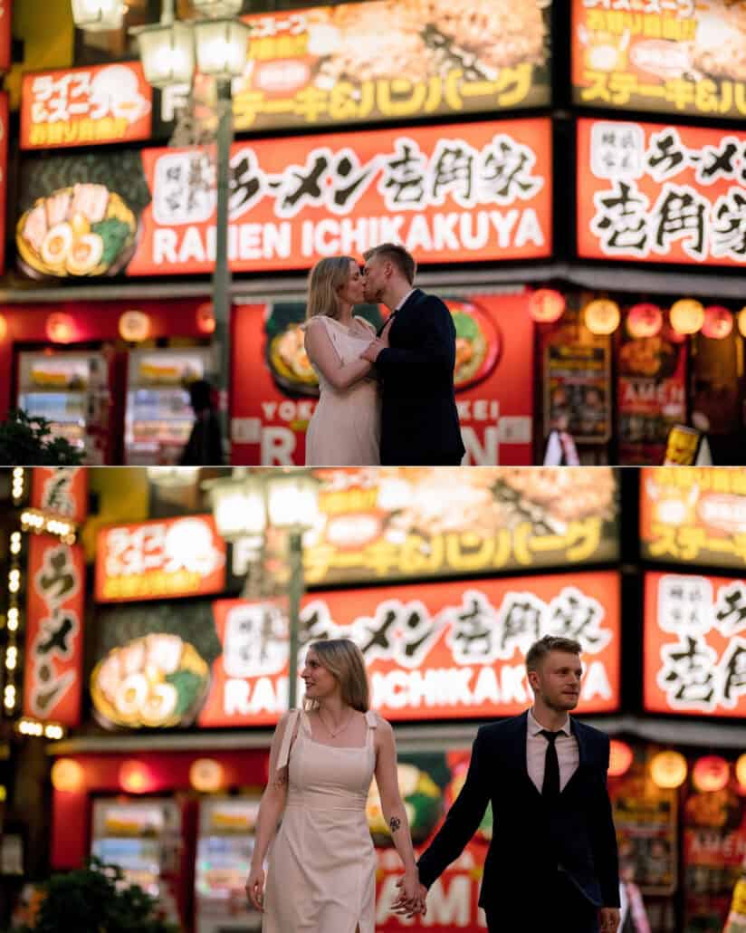 The couple kiss beneath giant neon ramen signs, then walk hand in hand past them, Shinjuku street photography before their elopement in Japan.