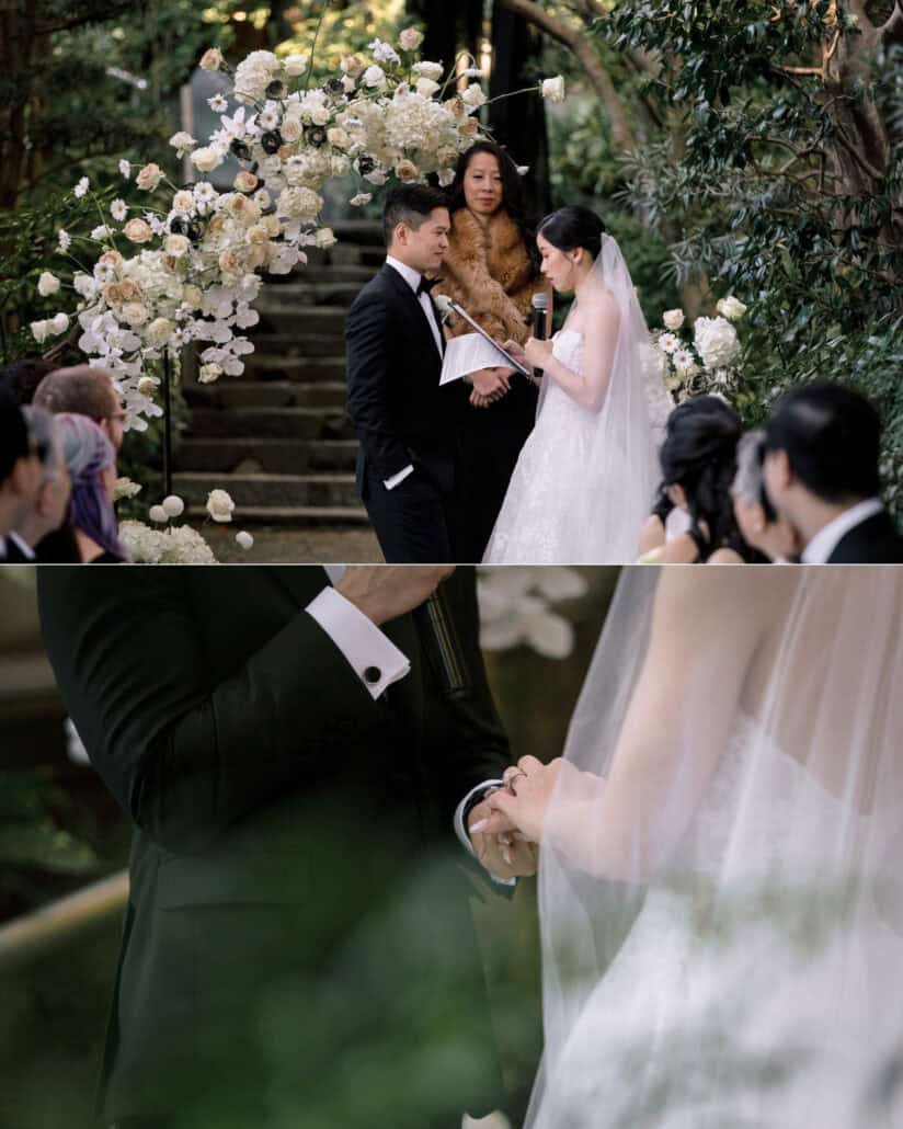 The bride's friend in a fur stole leads their garden ceremony under a white floral arch at Jinya as the bride speaks, then the couple hold hands.