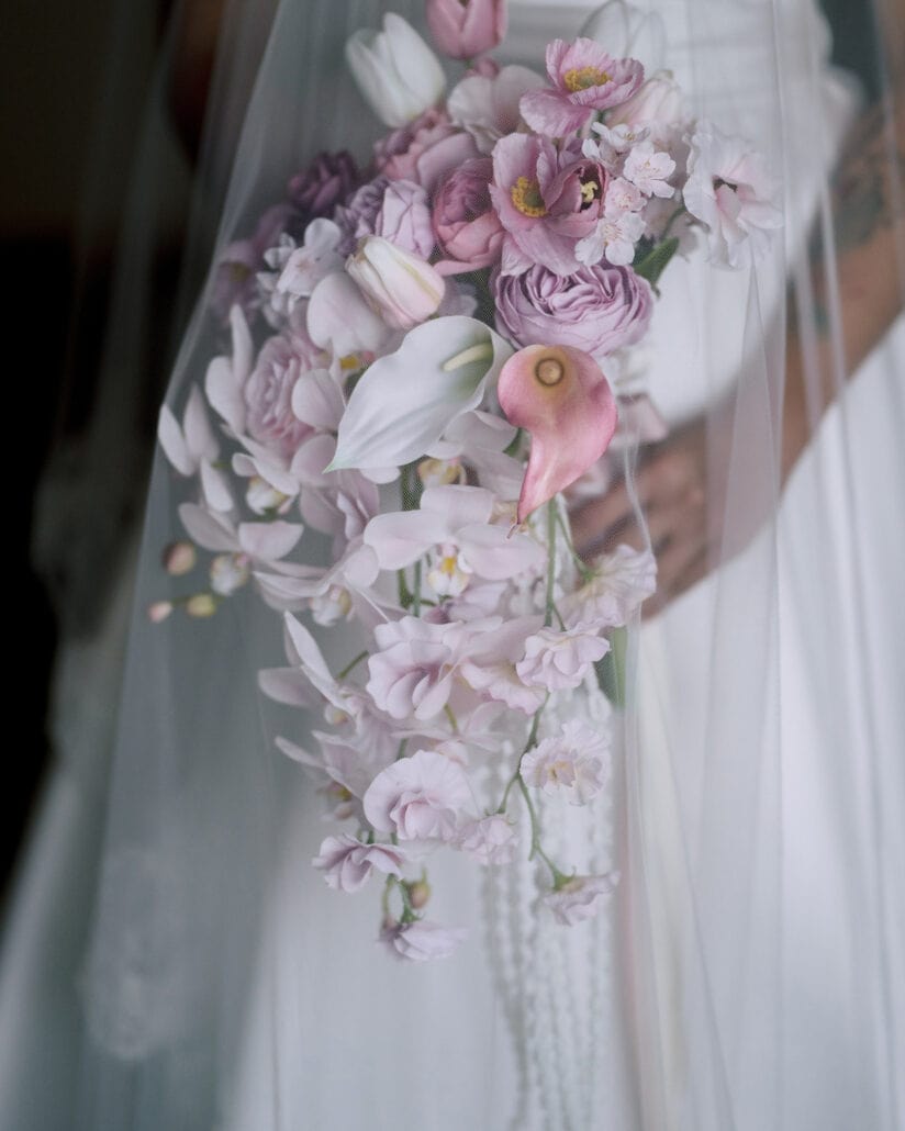 Her cascading bridal bouquet of pink roses, tulips, calla lilies and orchids against the white satin of her wedding dress.