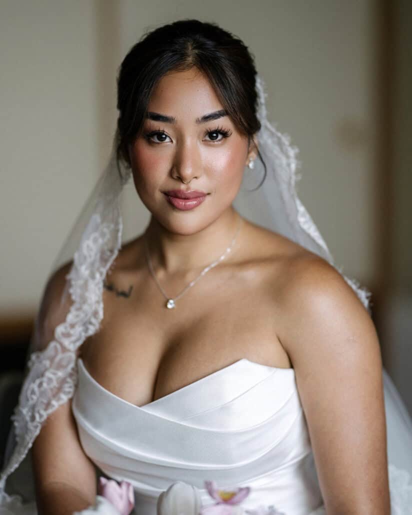 The bride in her lace mantilla veil holds pink tulips and looks straight at the camera, ready for her cherry blossom wedding.