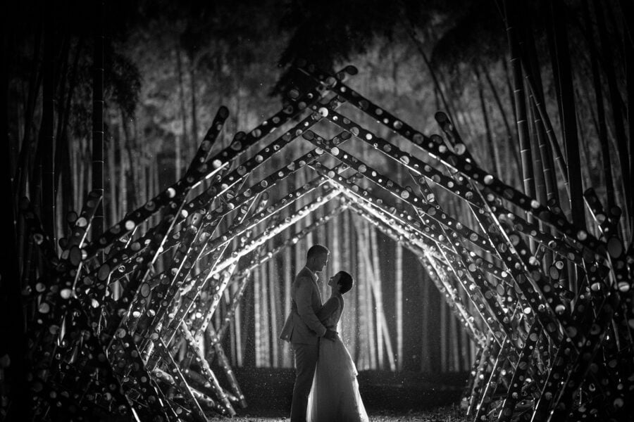 Silhouetted in the rain under a tunnel of drilled bamboo lit from inside, the couple face each other in the Wakayama Farm bamboo forest at night.