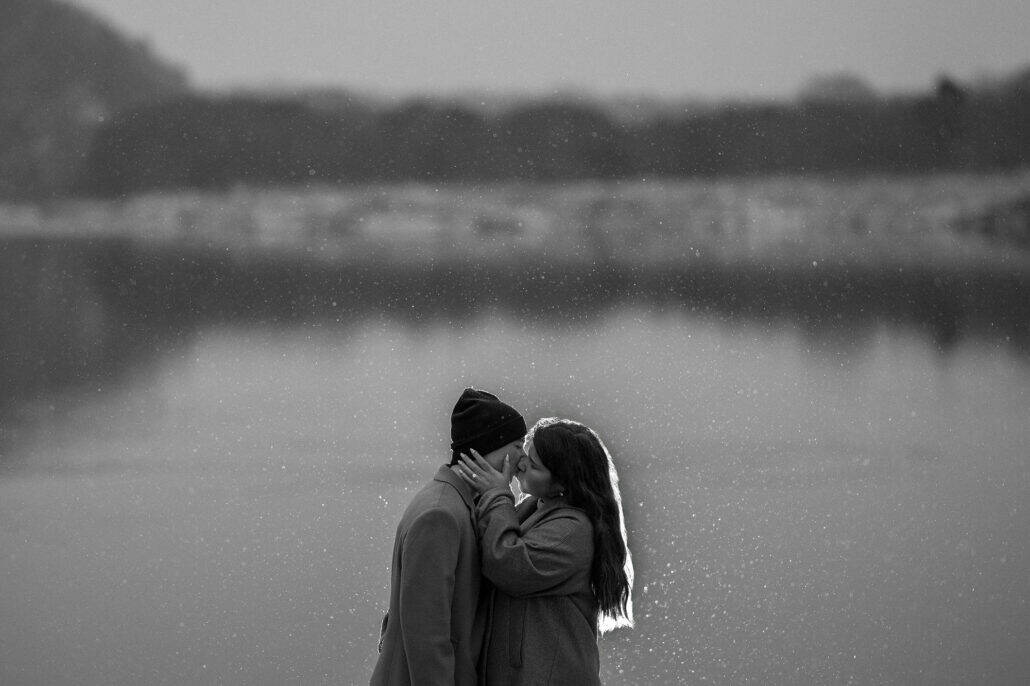 Snow falls across the lake behind them as they kiss, her hand with its new ring on his cheek, in black and white after the winter proposal.