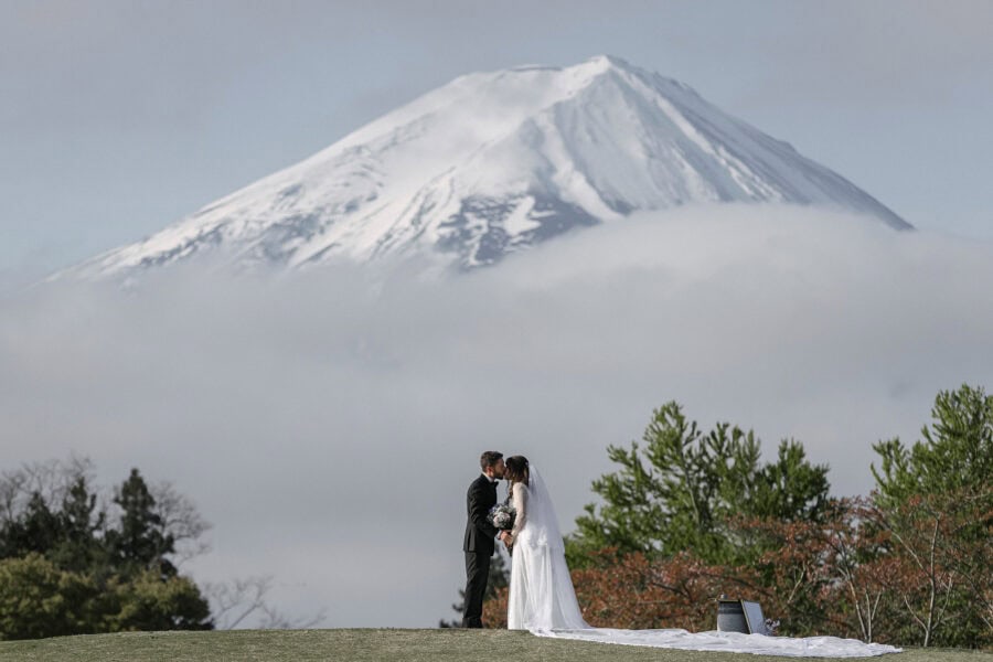 The couple kiss on a lawn by Lake Kawaguchi as Mt Fuji's summit rises out of a sea of cloud, at the end of their spring elopement vows.