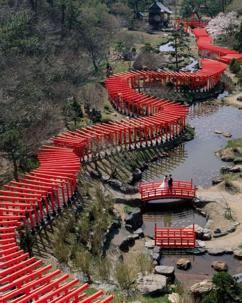 From above, the couple stand on a red bridge as rows of torii zigzag through the garden of Takayama Inari Shrine.