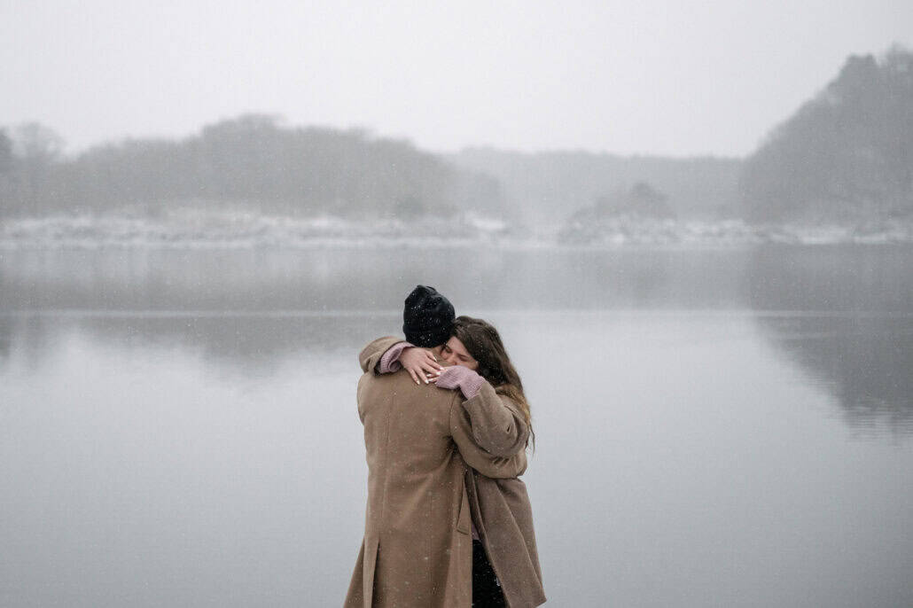 Eyes closed, she wraps her arms around his neck as snow falls over Lake Shoji and its misty hills, a winter proposal in Japan.