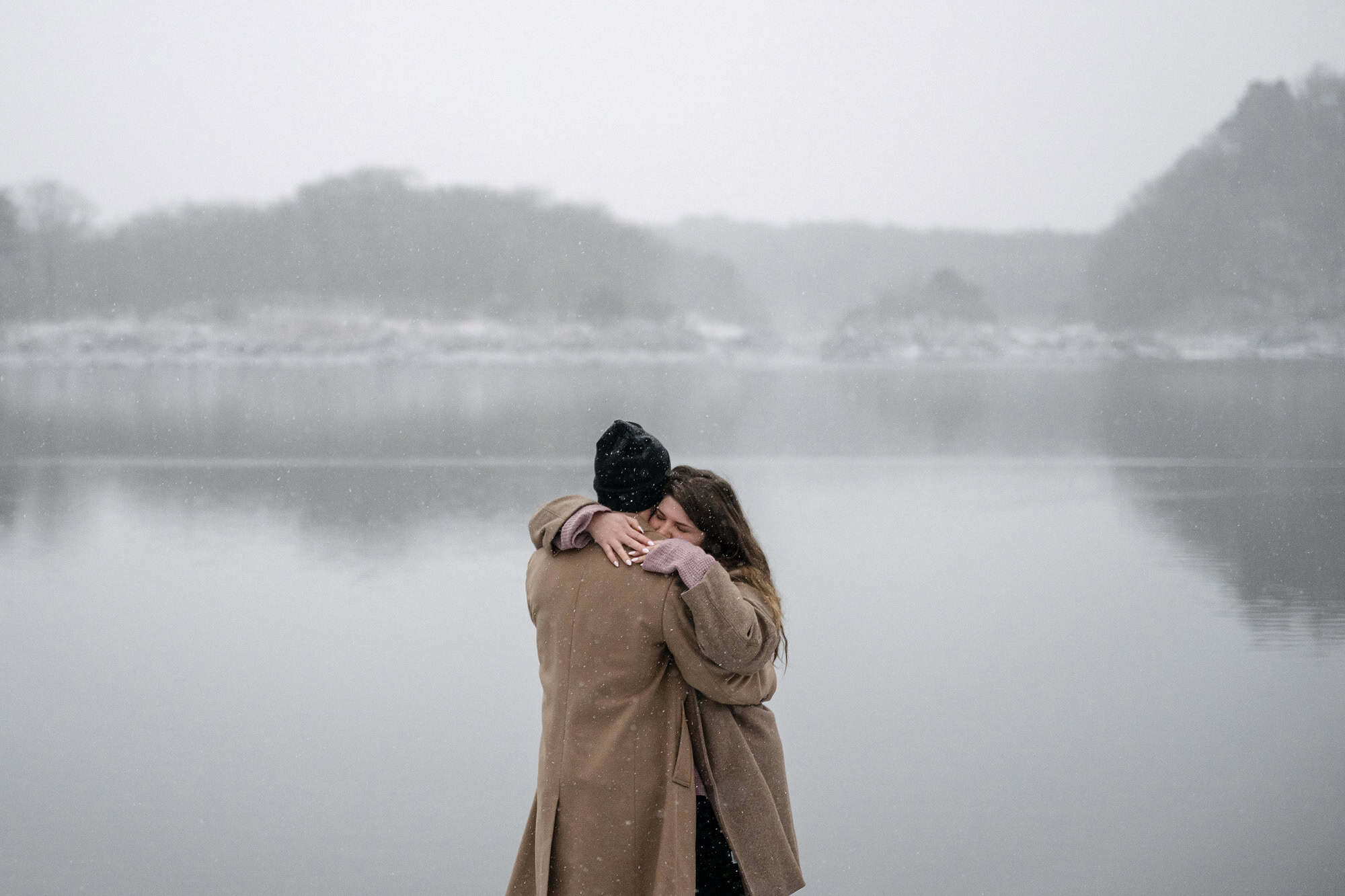 Eyes closed, she wraps her arms around his neck as snow falls over Lake Shoji and its misty hills, a winter proposal in Japan.