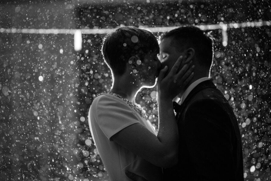 The bride holds the groom's face as they kiss after dark, rain lit up behind them, at their intimate wedding in Japan.