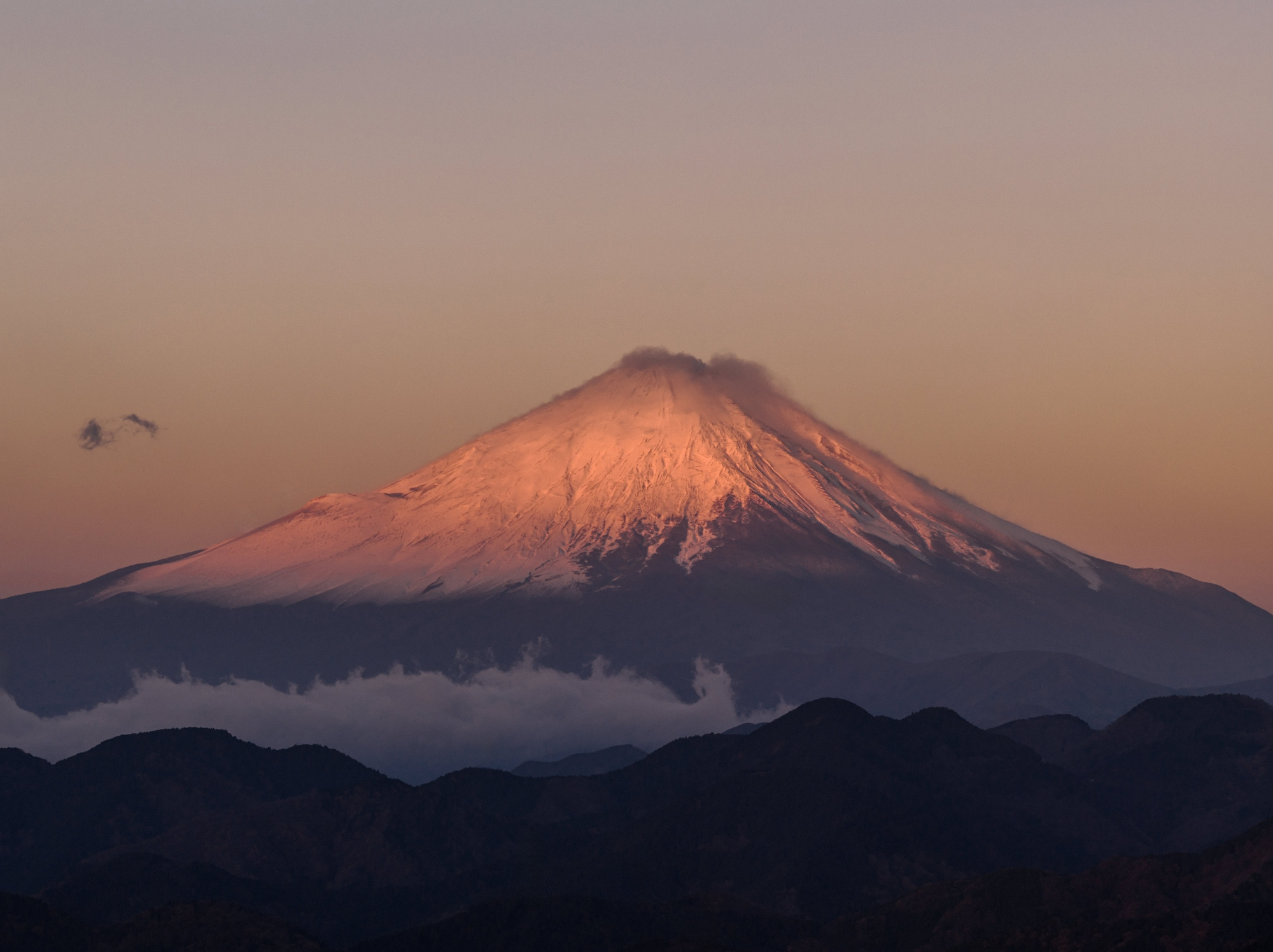 Mt Fuji glows red with snow at sunrise above blue ridges on the morning of a late autumn wedding in Japan.