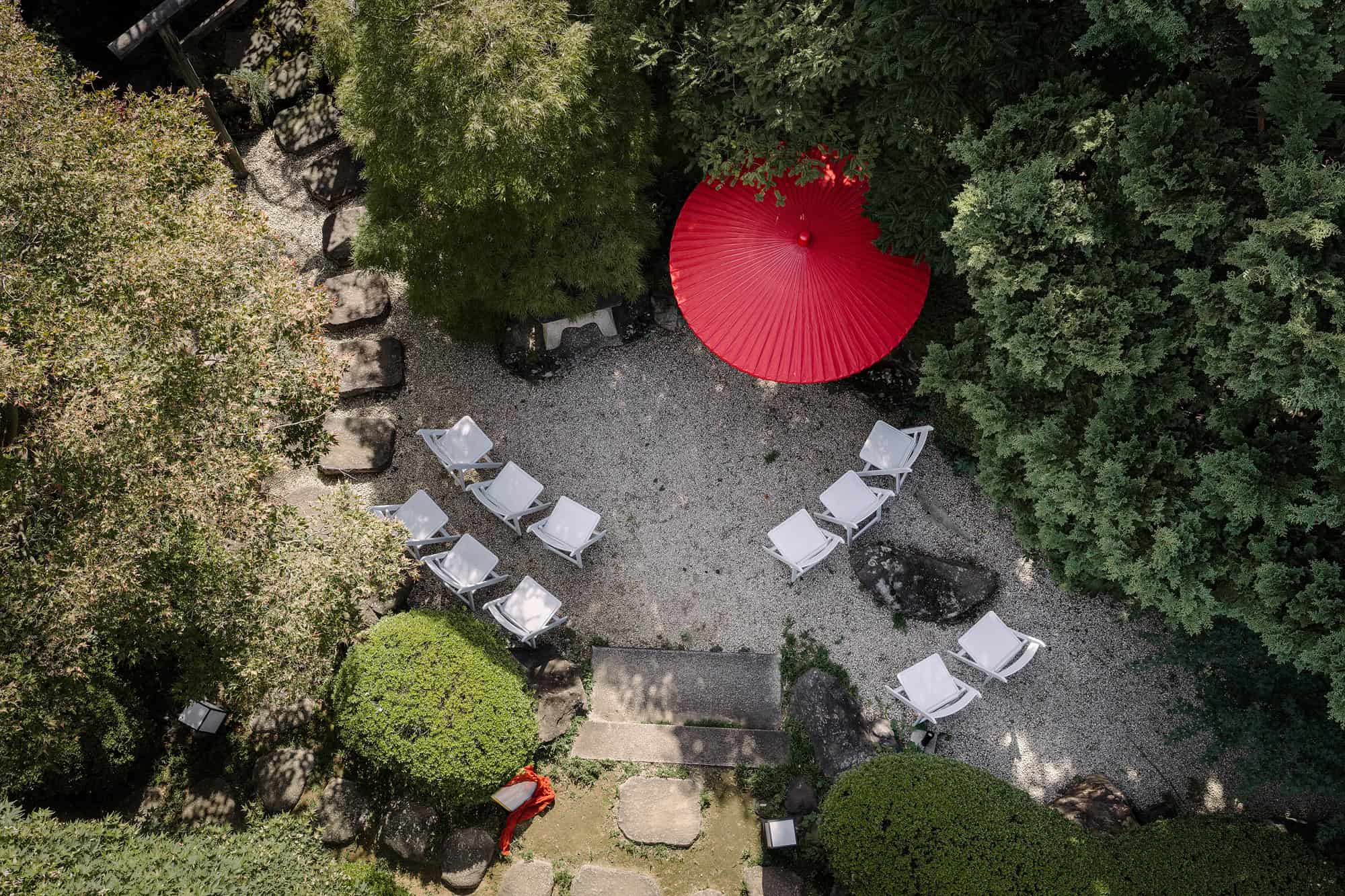 From above, white chairs face a red wagasa in the raked gravel of a Kawagoe garden, set for a small Japanese garden wedding.