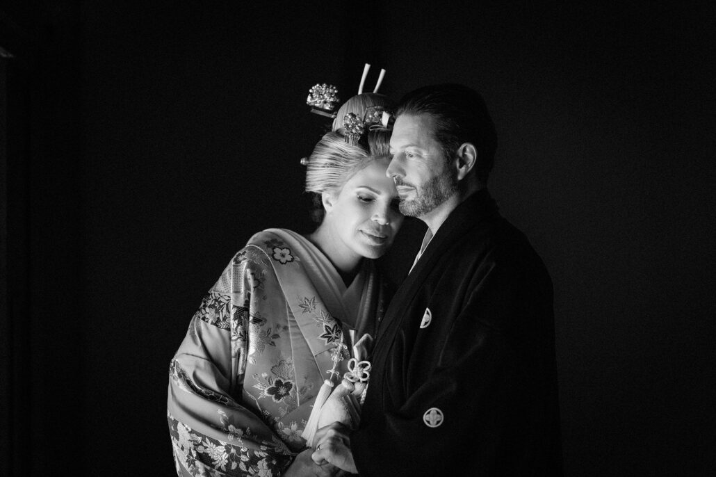 Black and white portrait of a bride in nihongami and patterned kimono resting her head against her groom in a black crested kimono