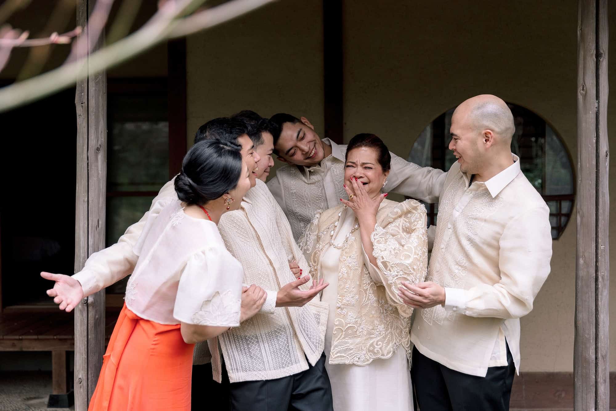 Family in white barong and butterfly sleeves laugh together on a veranda, each dressed as themselves for a wedding in Japan at Tsurumaki Onsen.