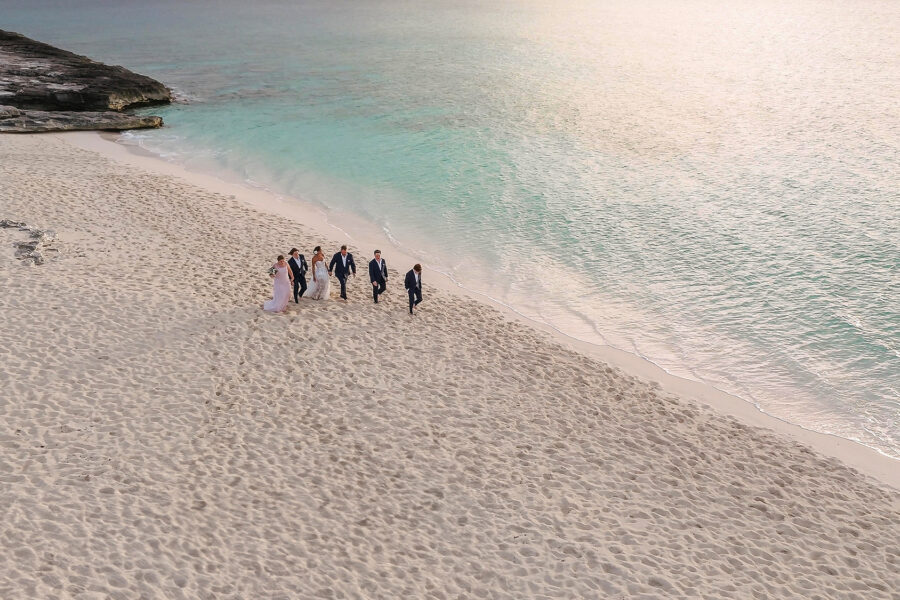 Seen from above, the couple and their four children walk along a wide white sand beach beside turquoise shallows at Amanyara.