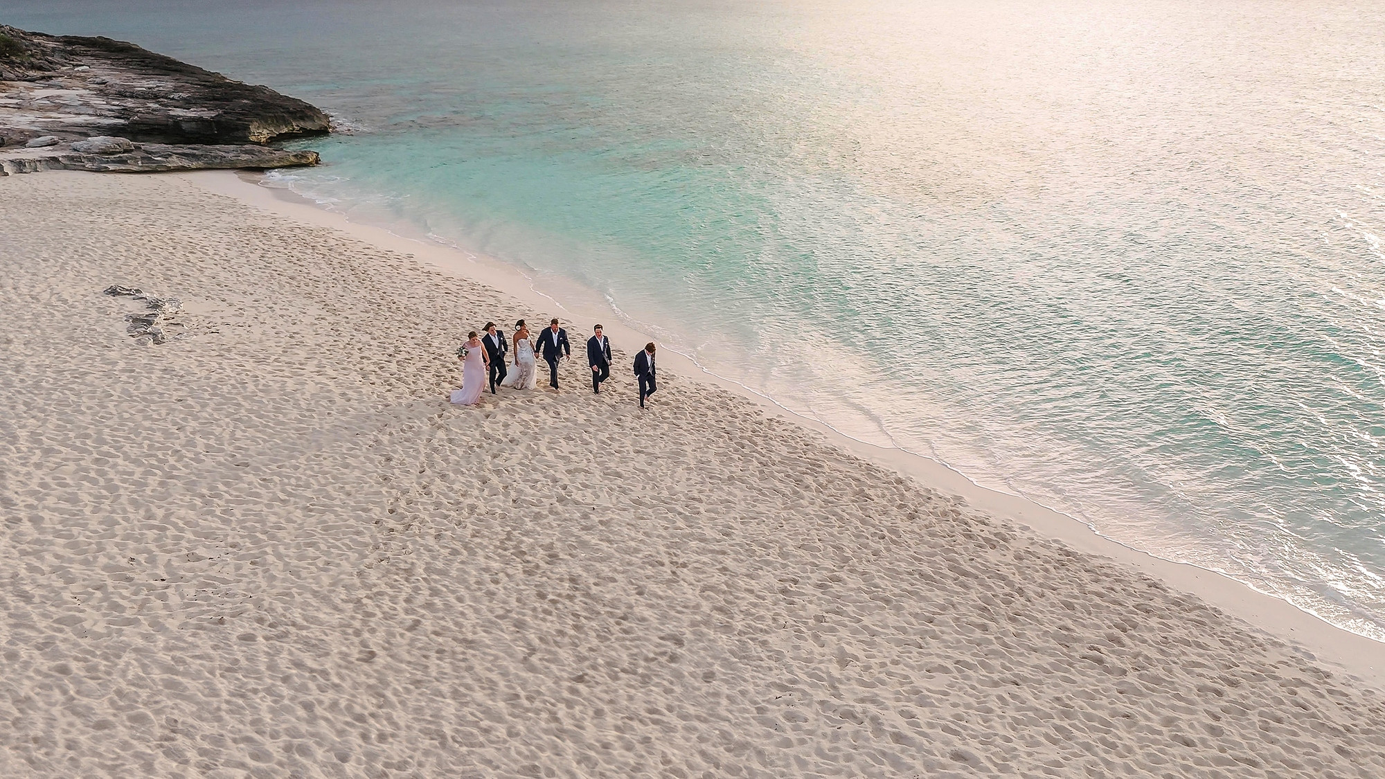 Seen from above, the couple and their four children walk along a wide white sand beach beside turquoise shallows at Amanyara.