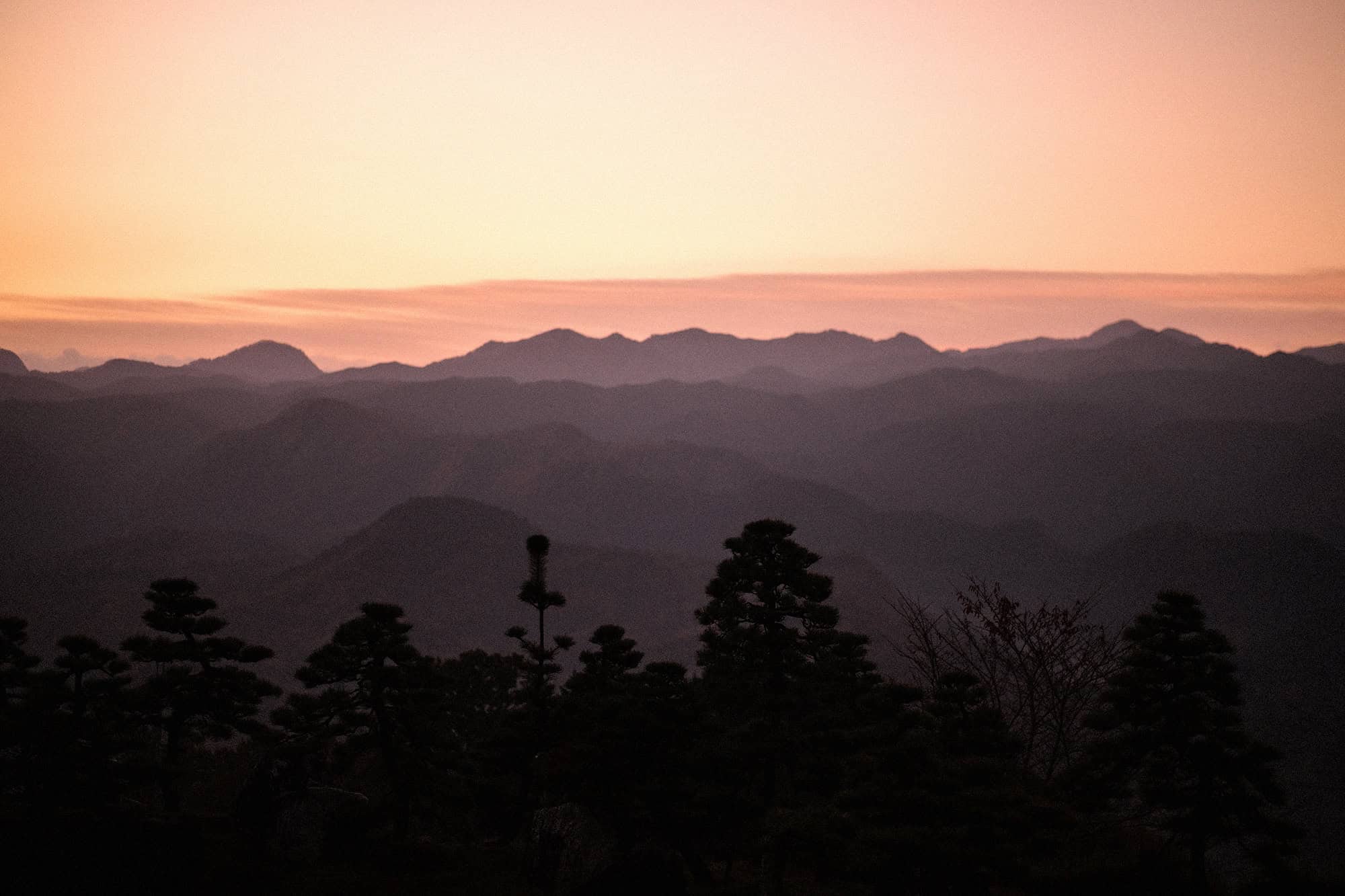 Sunrise turns the sky pink over ridge after ridge of mountains in Uda, seen from a villa in Nara on the morning of an elopement in Japan.