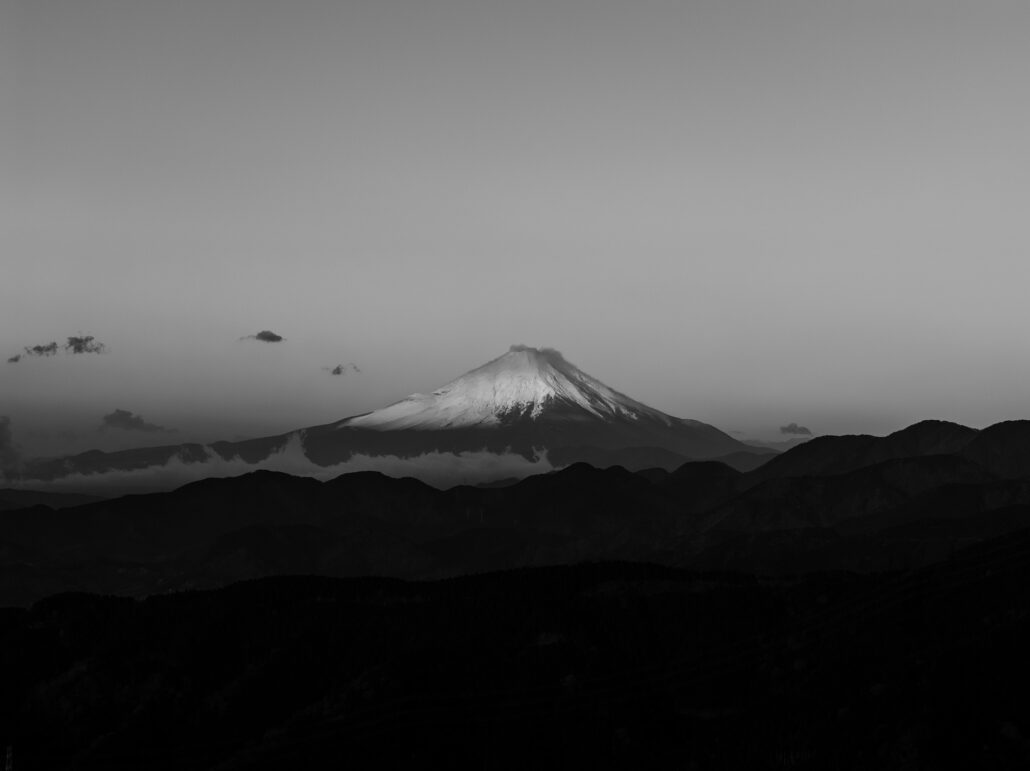 Mt Fuji capped with snow rises over layered ridges at dawn in a black and white frame from a wedding morning.