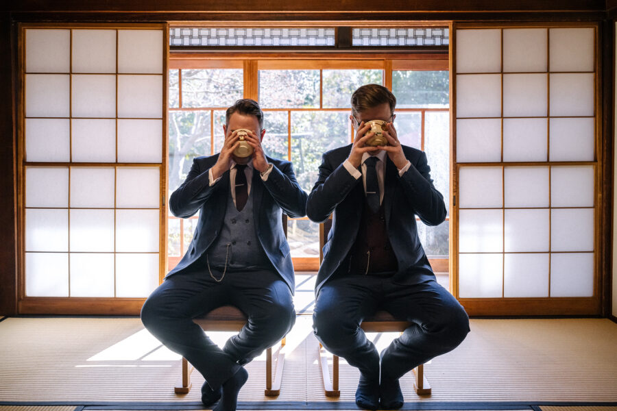 Two grooms drink matcha in the same moment against glowing shoji at Tantoku in Kawagoe, a tea ceremony wedding in Japan.