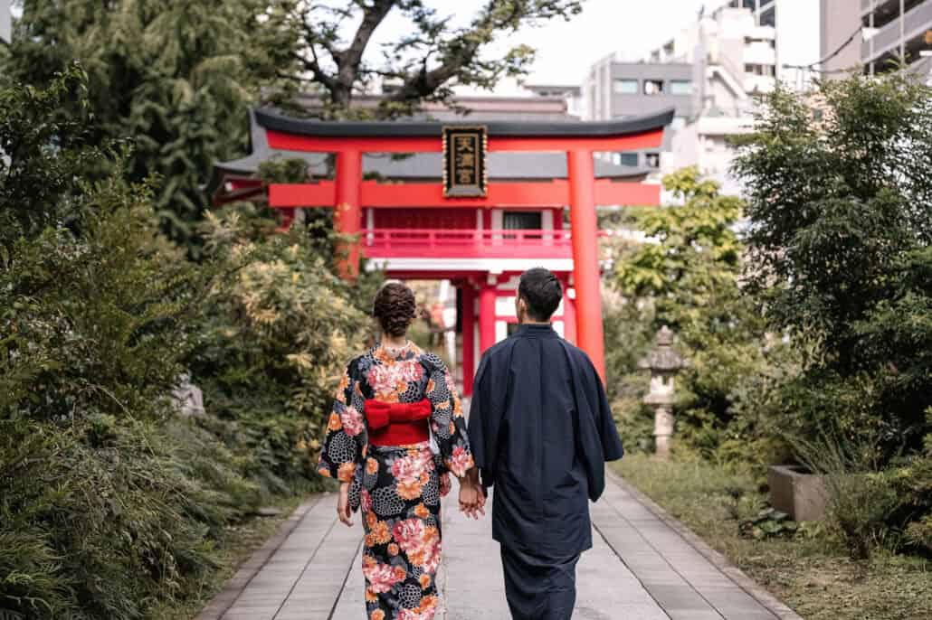 In kimono, the couple walk hand in hand toward the vermilion torii and gate of Naruko Tenjin Shrine in Shinjuku, Tokyo.