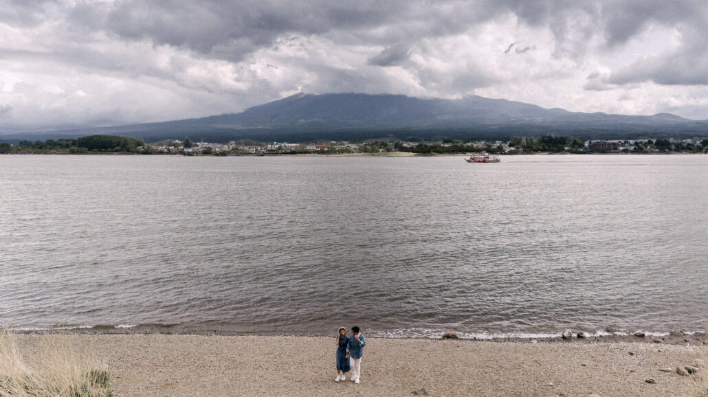 Lake Kawaguchi stretches to a low band of Mt Fuji and cloud, the couple a tiny pair on the empty beach in the foreground.