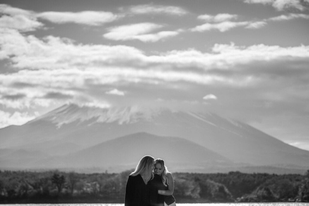 In black and white, one leans into the other on the shore of Lake Shoji, Mt Fuji and Omuro-yama rising behind under drifting cloud.