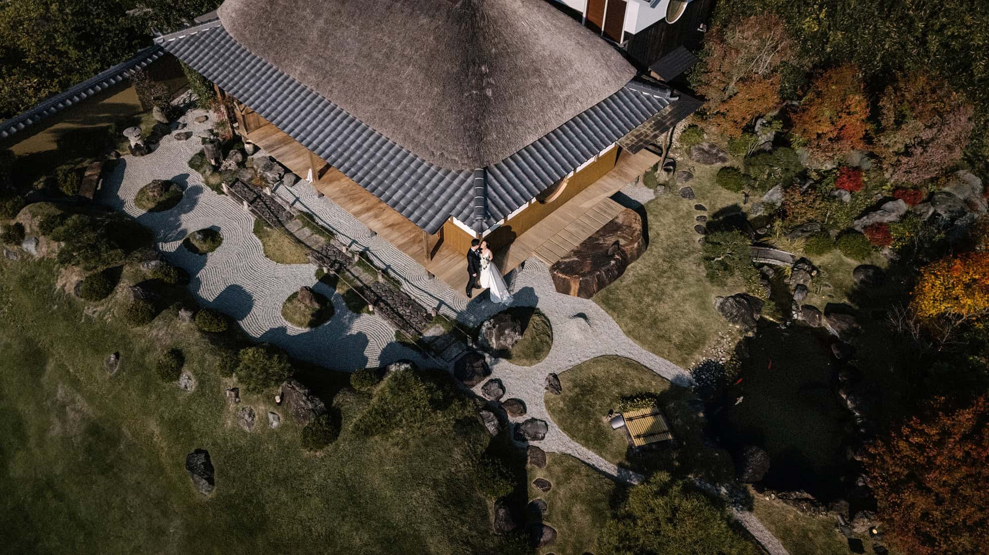 From above, a thatched teahouse with raked gravel, a rock garden and autumn maples at a private villa for an elopement in Japan, in Nara.