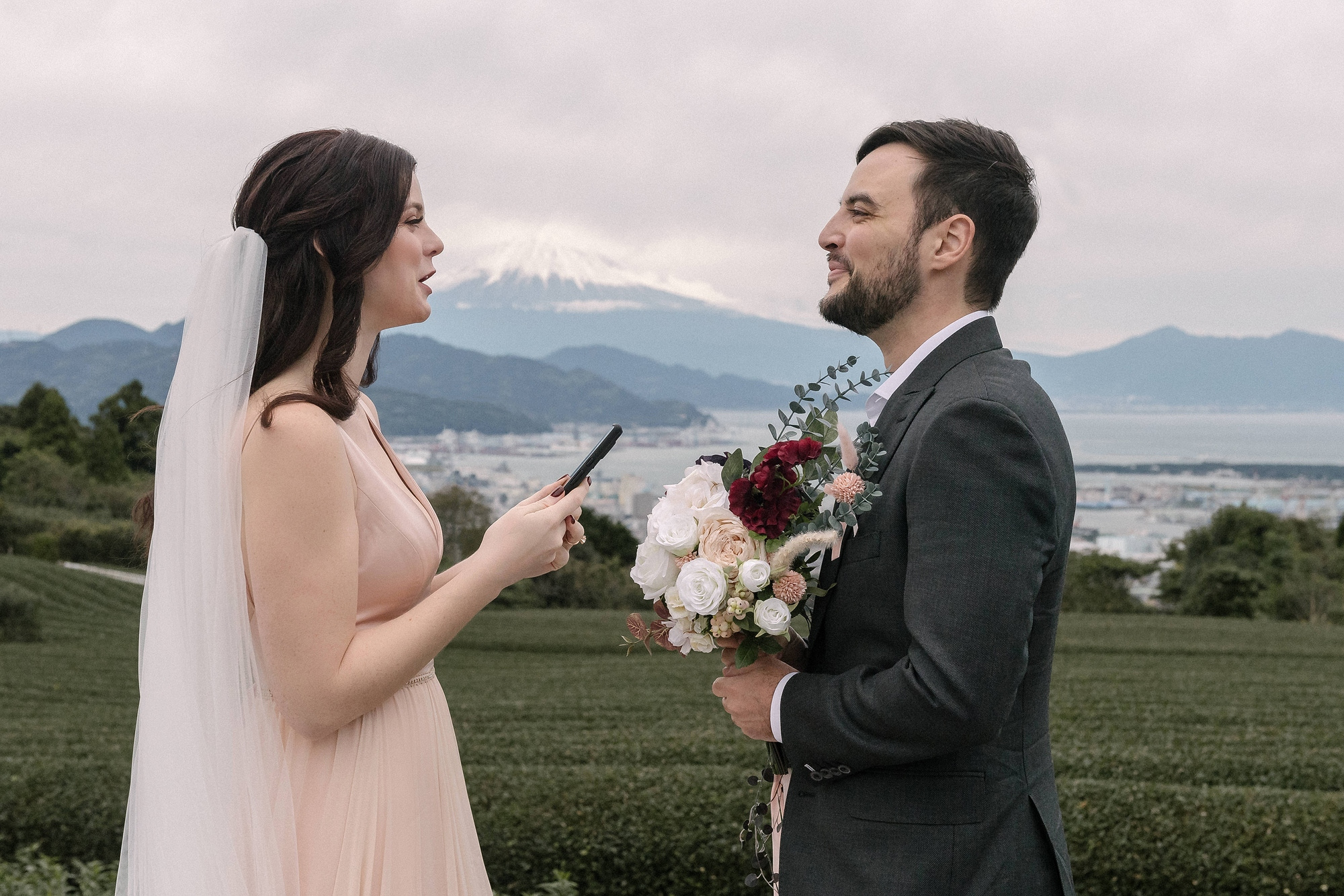 A bride reads her vows on a tea deck above Shizuoka, Mt Fuji faint over the city and the bay, at an elopement in Japan planned around the season.