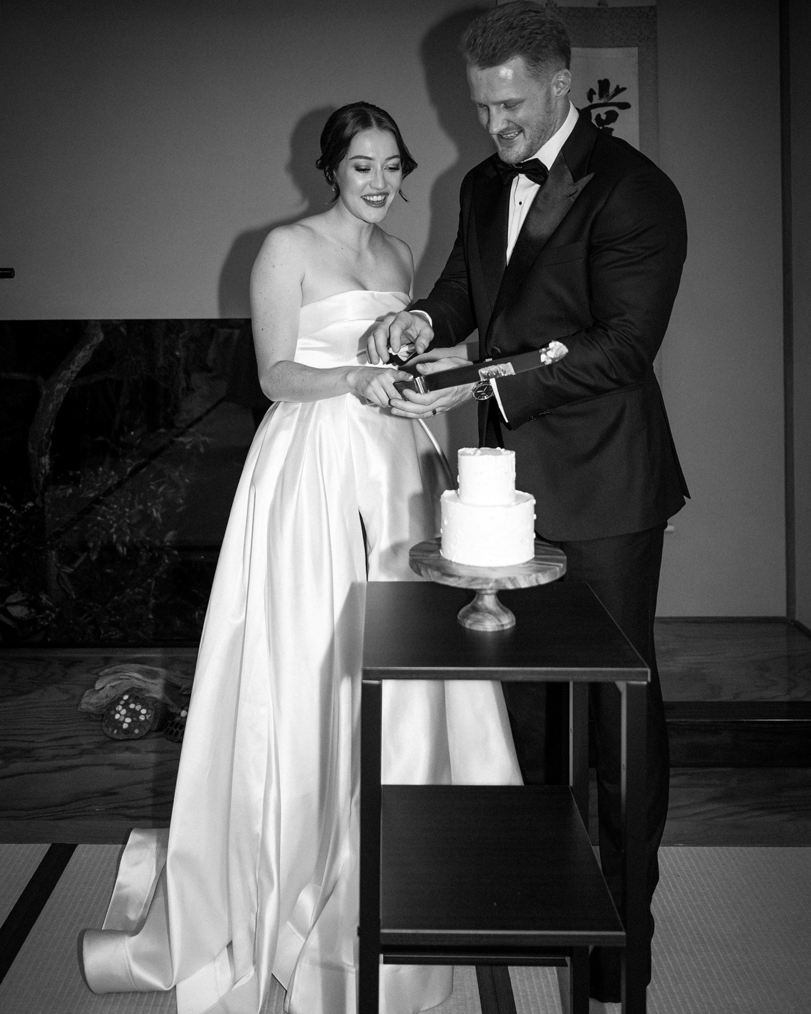 In black and white, the bride and groom cut a small two-tier white wedding cake together in a tatami room at a ryokan wedding in Kanagawa.