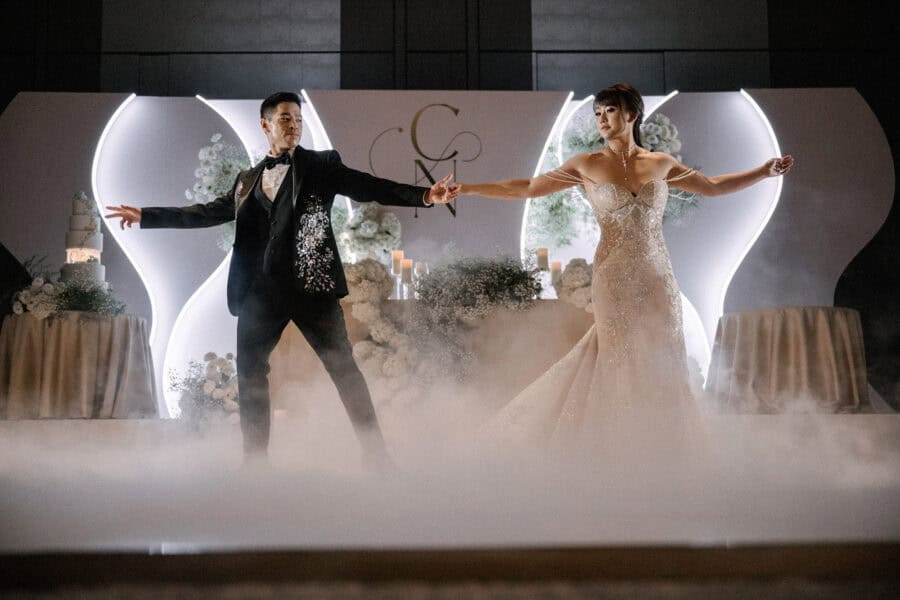The groom and bride stretch out their arms hand in hand across a fog-covered dance floor during their first dance at a Tokyo hotel wedding.