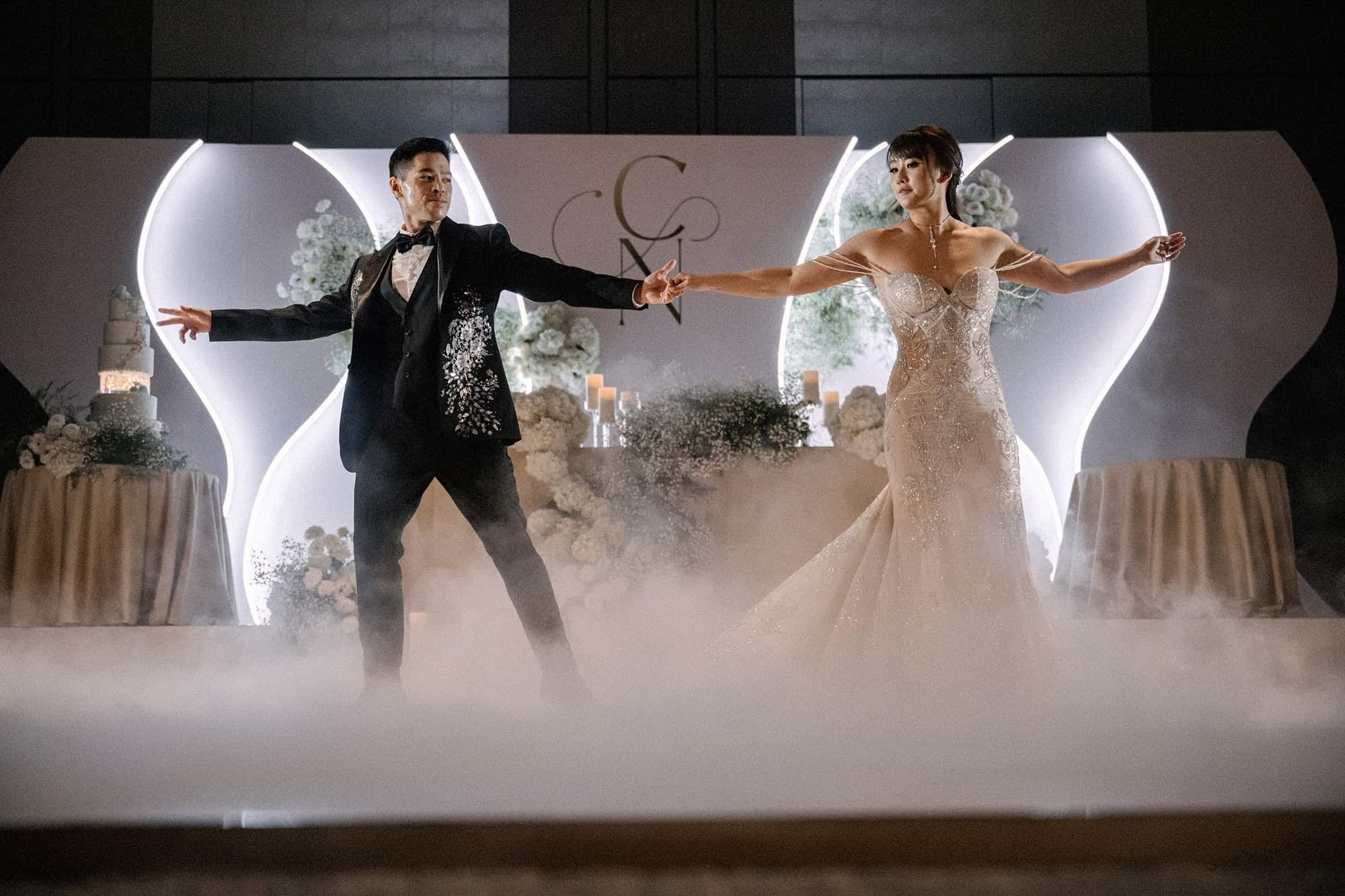 The groom and bride stretch out their arms hand in hand across a fog-covered dance floor during their first dance at a Tokyo hotel wedding.