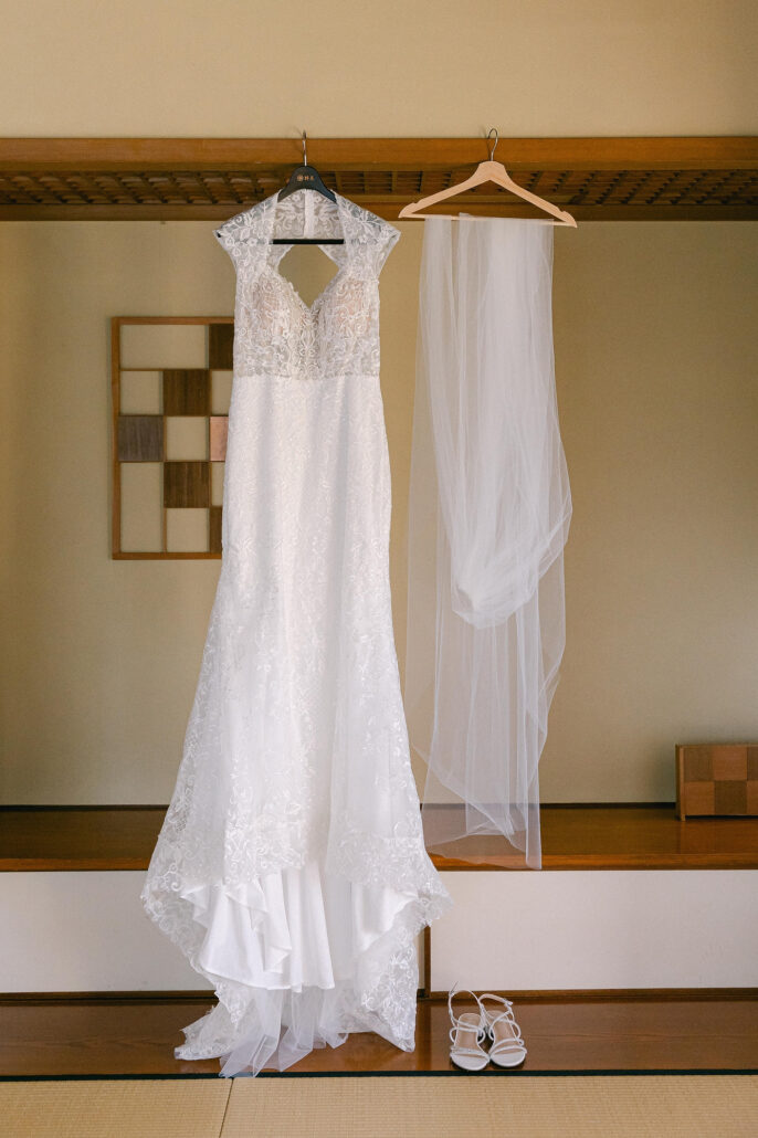 The wedding dress and veil hang from a wooden rail in a tatami room at Jinya Ryokan, with her sandals on the floor beneath.