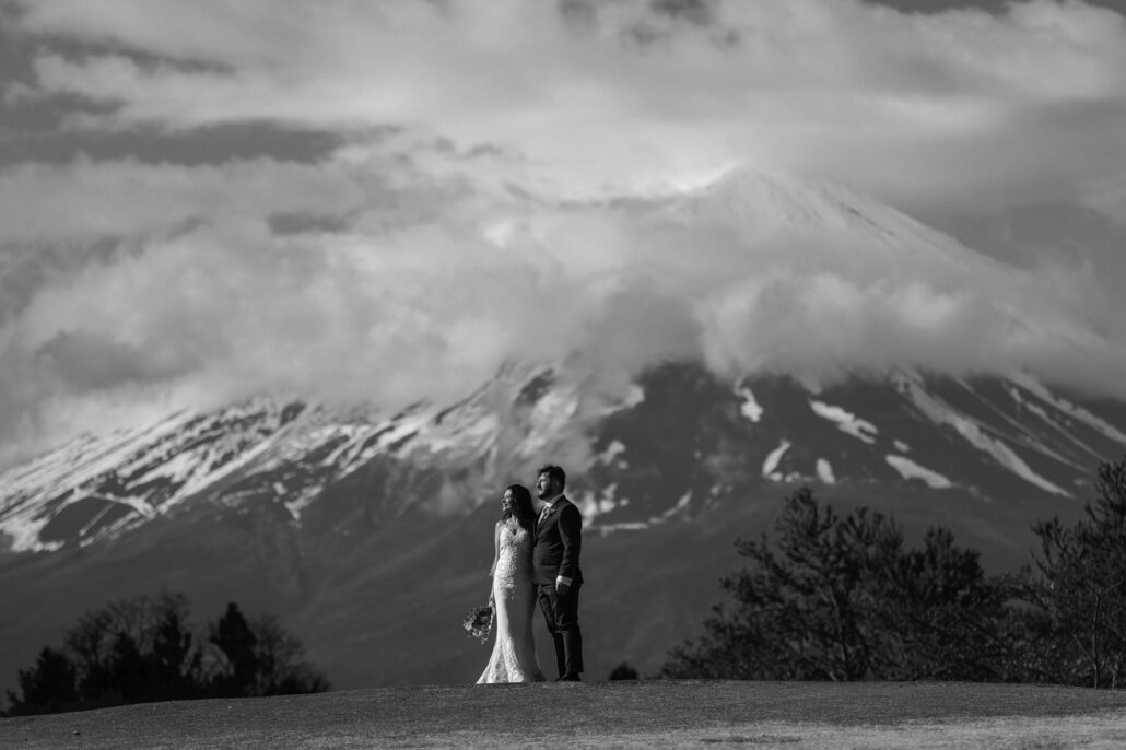 In black and white, the couple stand close beneath the snow streaked slopes of Mt Fuji as cloud rolls over the top.