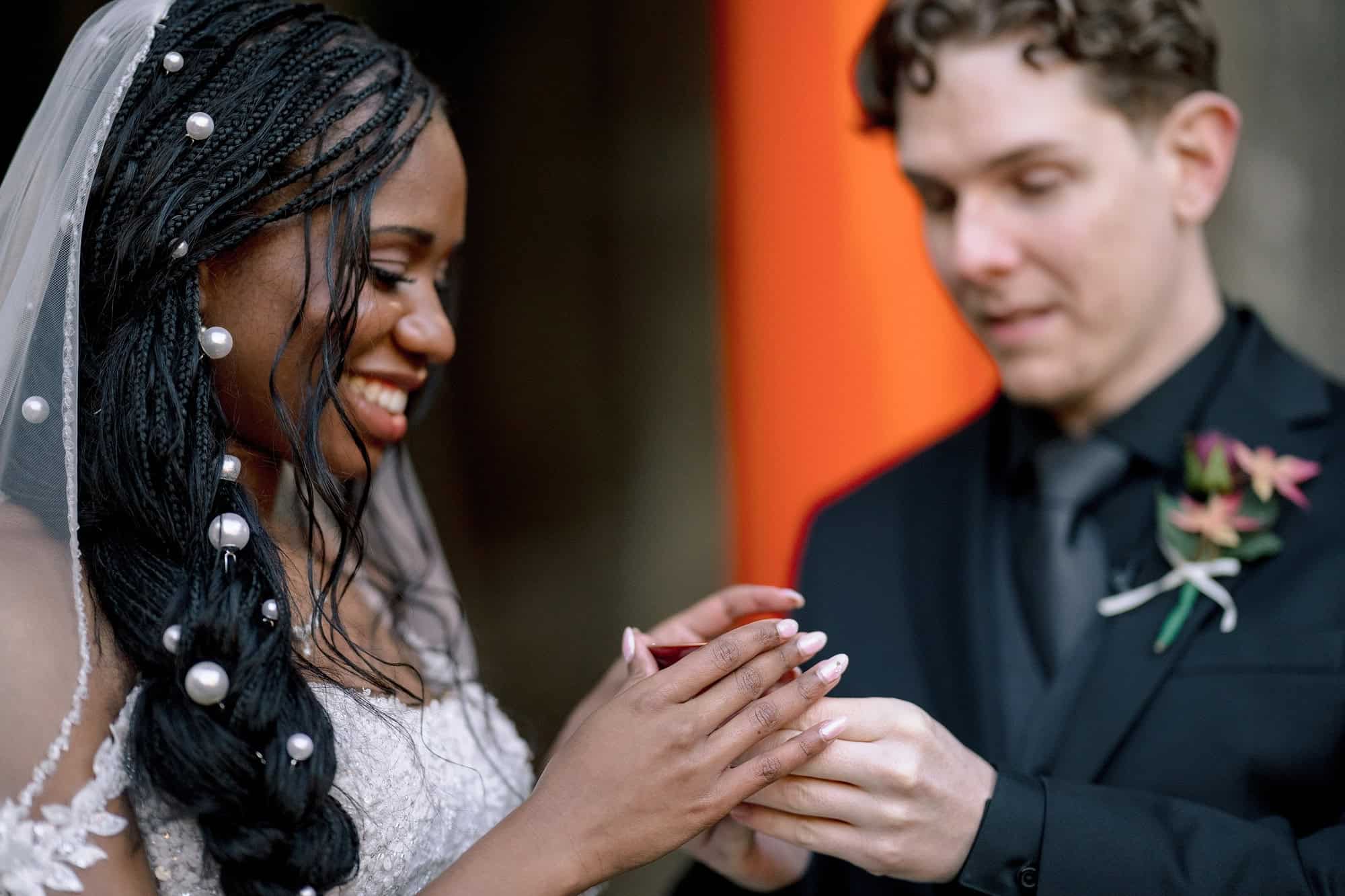 A bride smiles and holds a small red lacquer sake cup in both hands as the groom looks on, sharing san-san-kudo in a private garden in Kyoto.