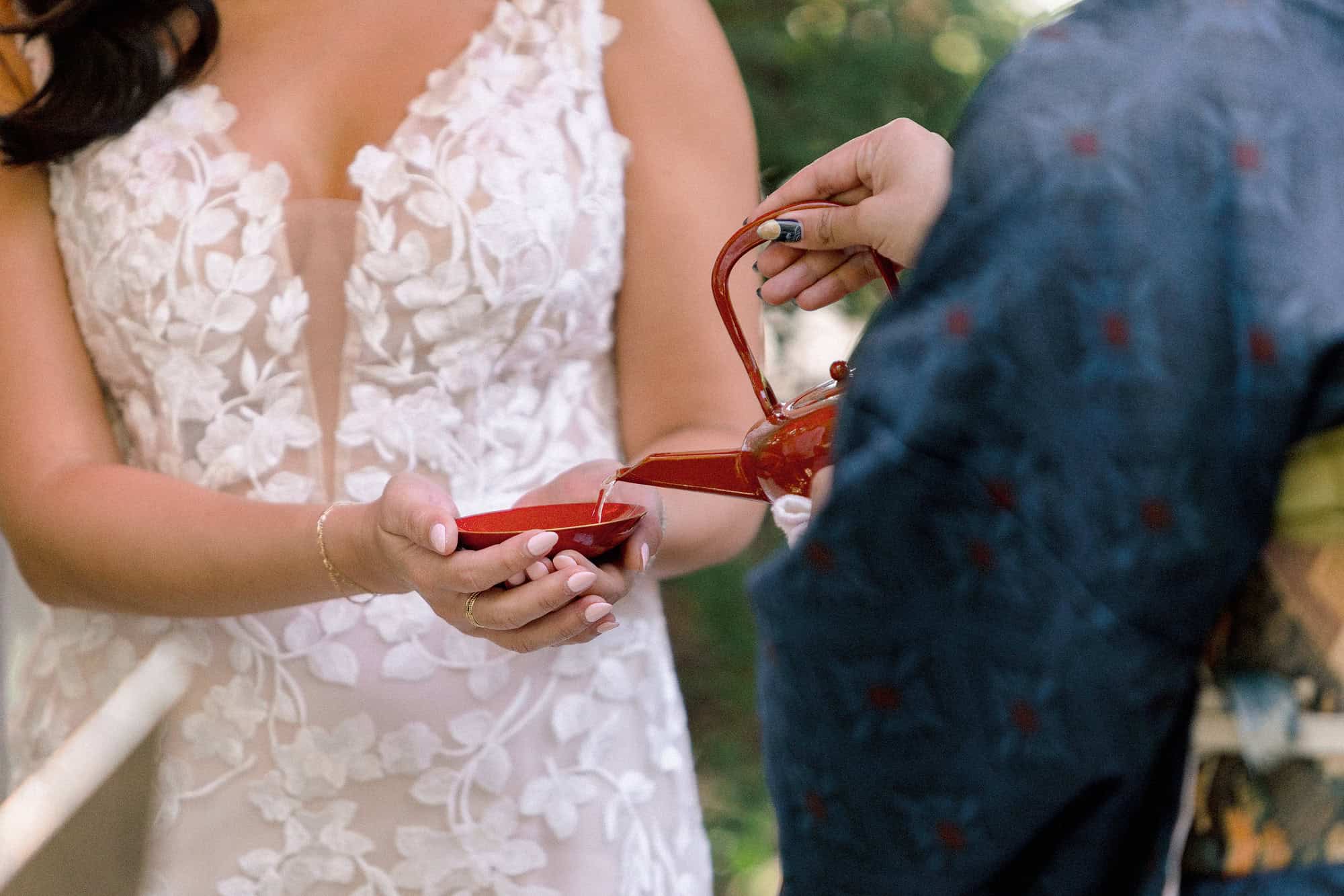 The bride holds a red lacquer sake cup in both hands during san-san-kudo in a Kawagoe garden, the Shinto three-cup rite carried into a ceremony of their own.