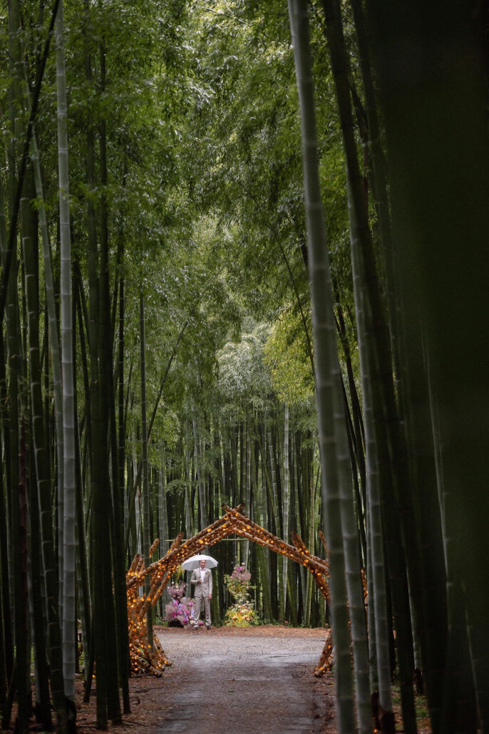 A gravel path runs through tall bamboo to a lit arch, set for an elopement ceremony in Japan.