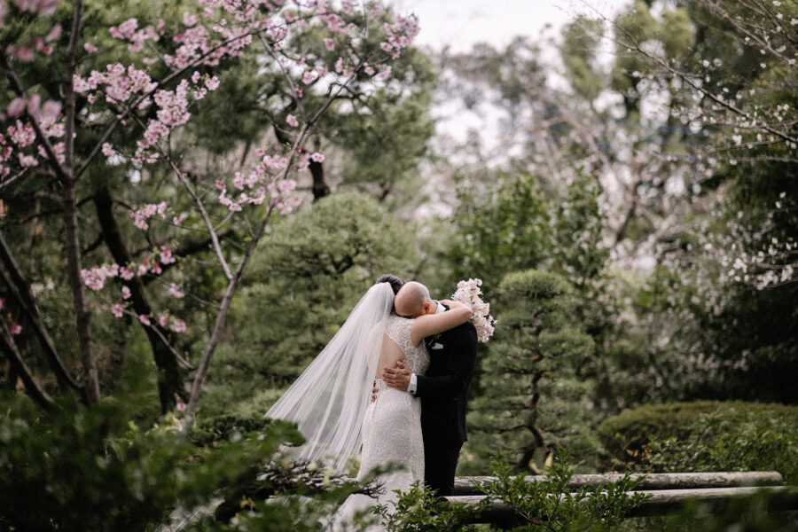 The bride and groom embrace in the garden after the first look, cherry blossom and pine around them at their spring wedding in Japan.