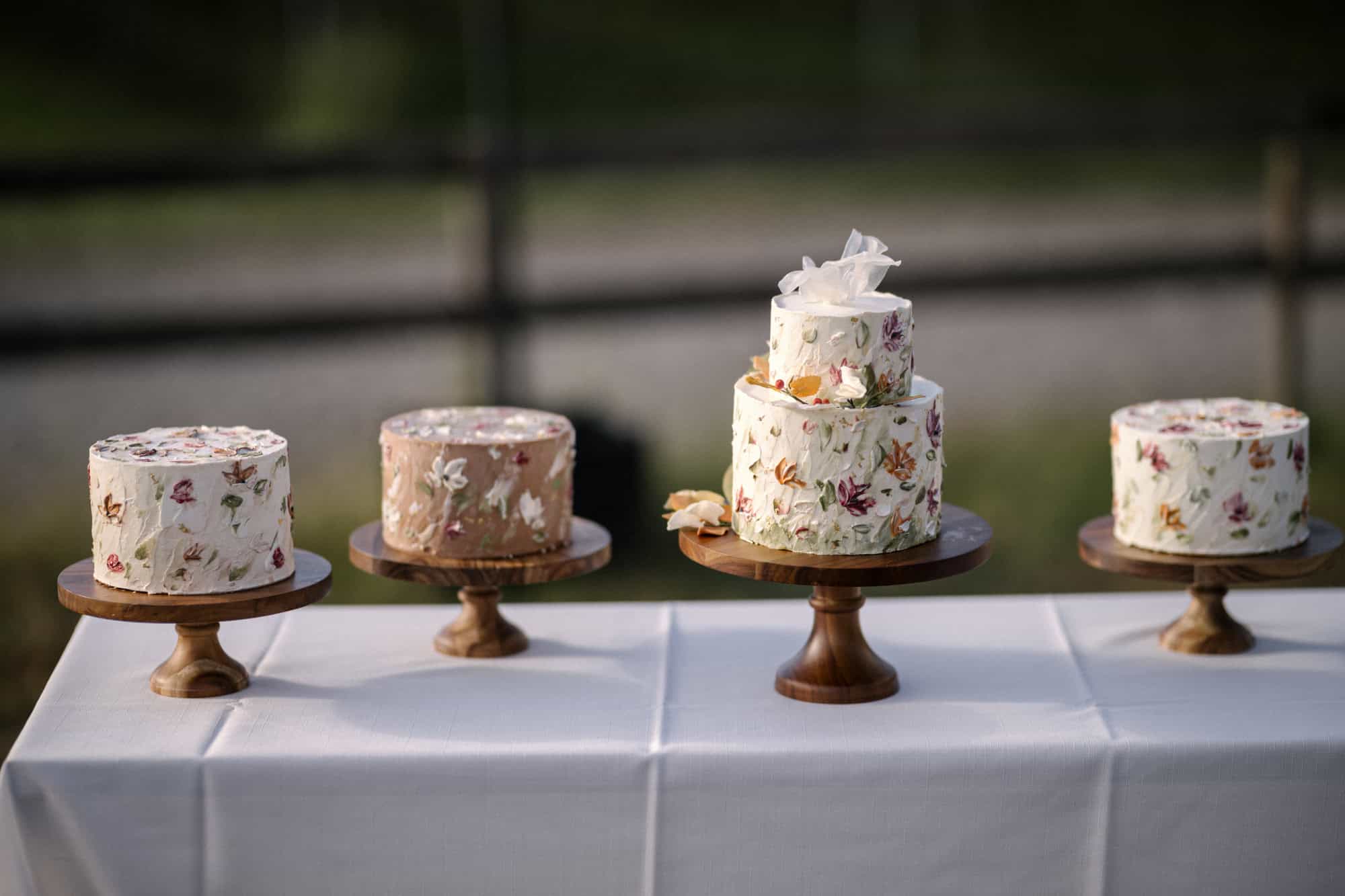 Four wedding cakes painted with autumn leaves stand in a row on wooden cake stands, one of them two tiers tall, at a winery wedding in Japan.