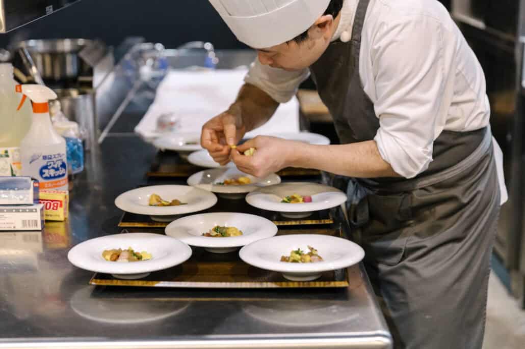 The chef plates a course of small dishes for the welcome dinner, the white plates lined up on the counter before they go to the table.