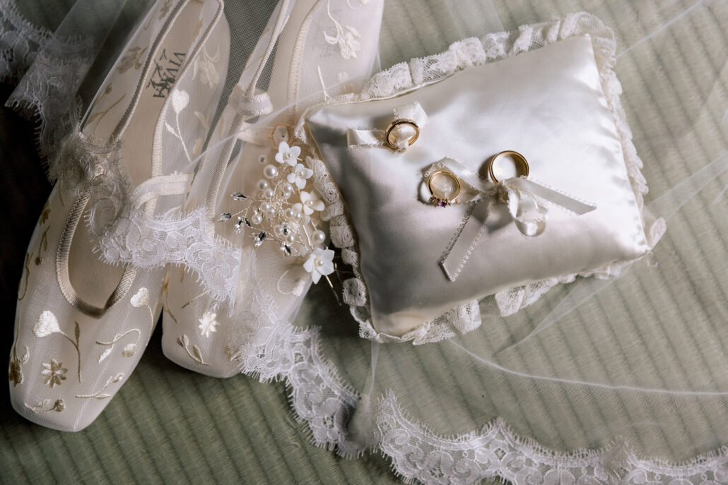 The bride's embroidered shoes, lace veil and a ring pillow holding both wedding rings, laid out on tatami.