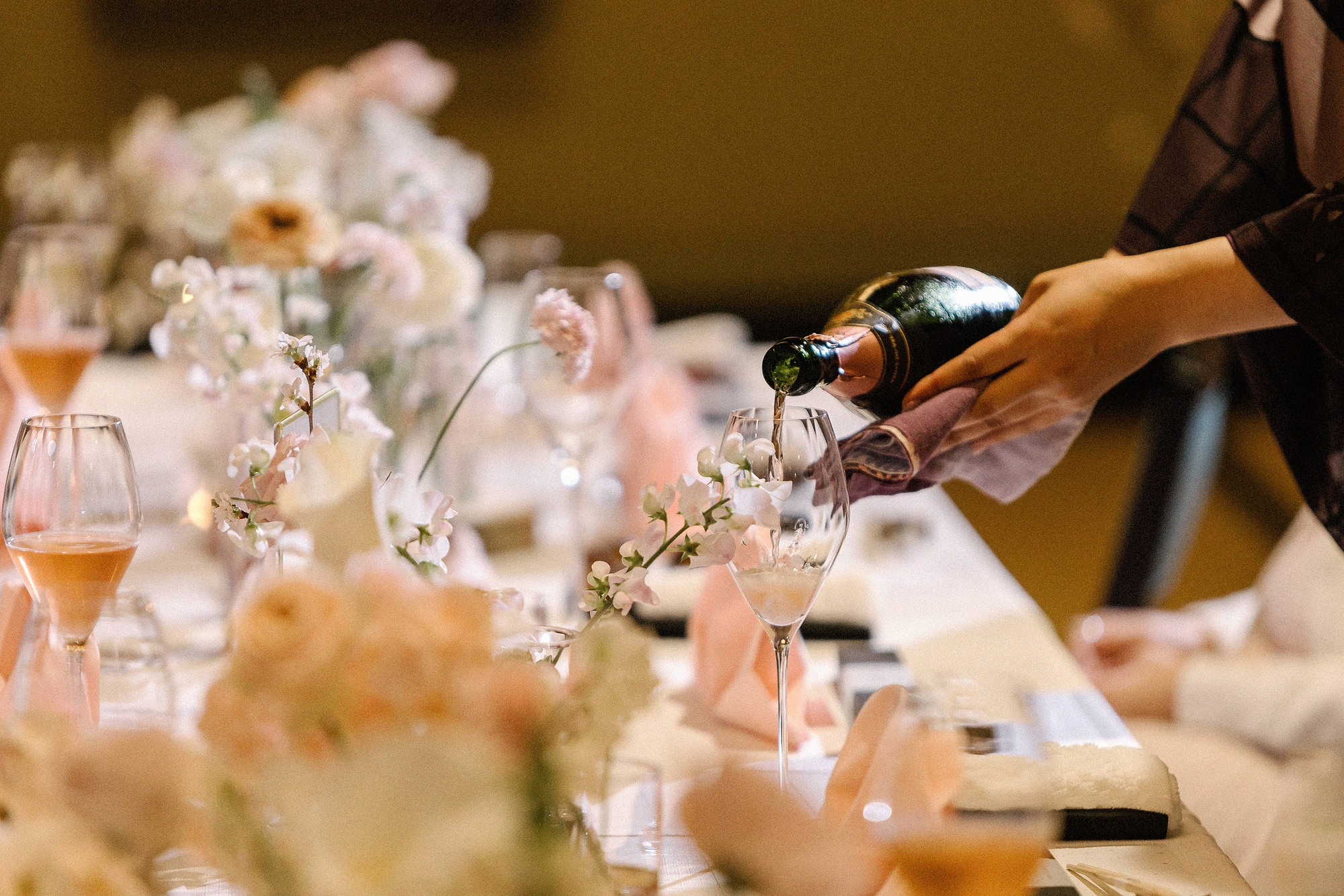 Champagne is poured at a ryokan wedding dinner, the long table set with peach flowers, blossom and rose-tinted glasses, for a small wedding in Japan.