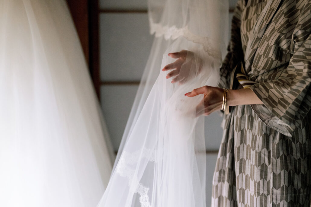 Close on the bride's hand touching the tulle of her wedding dress and veil.