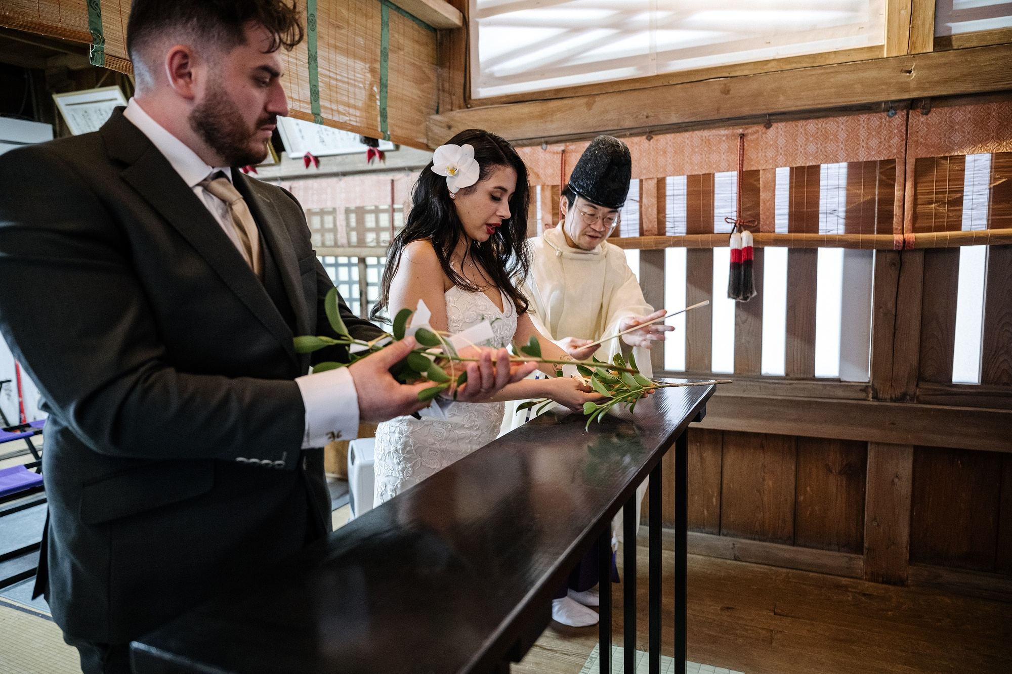 A bride and groom hold sprigs of evergreen sakaki while a priest guides them through the tamagushi offering at a Sengen shrine near Mt Fuji.