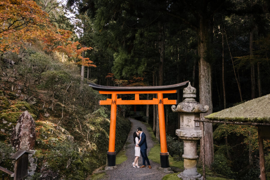 From above, the couple kiss beneath a red torii between a stone lantern and a moss-roofed pavilion at their private garden elopement in Kyoto.